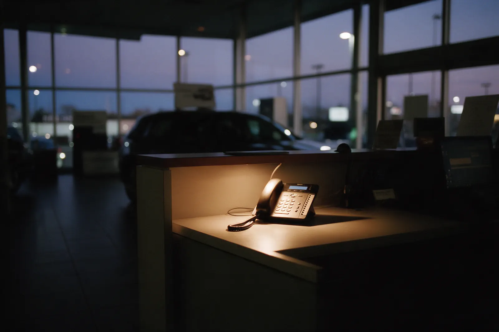 Dealership showroom after closing, the phone lit on the reception counter.